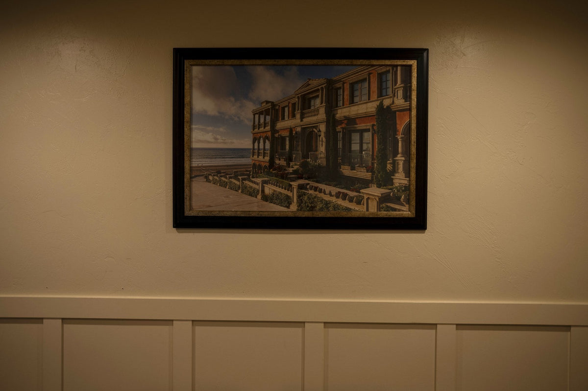 Framed landscape painting hanging level on a wall above white wainscoting