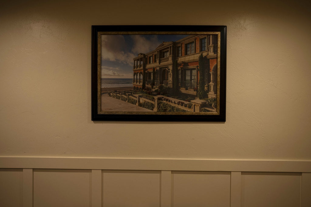 Framed landscape painting hanging level on a wall above white wainscoting