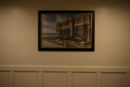 Framed landscape painting hanging level on a wall above white wainscoting